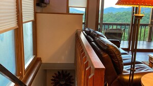 Una escalera con barandilla de madera que lleva a un balcón con un sofá de cuero y una mesa.