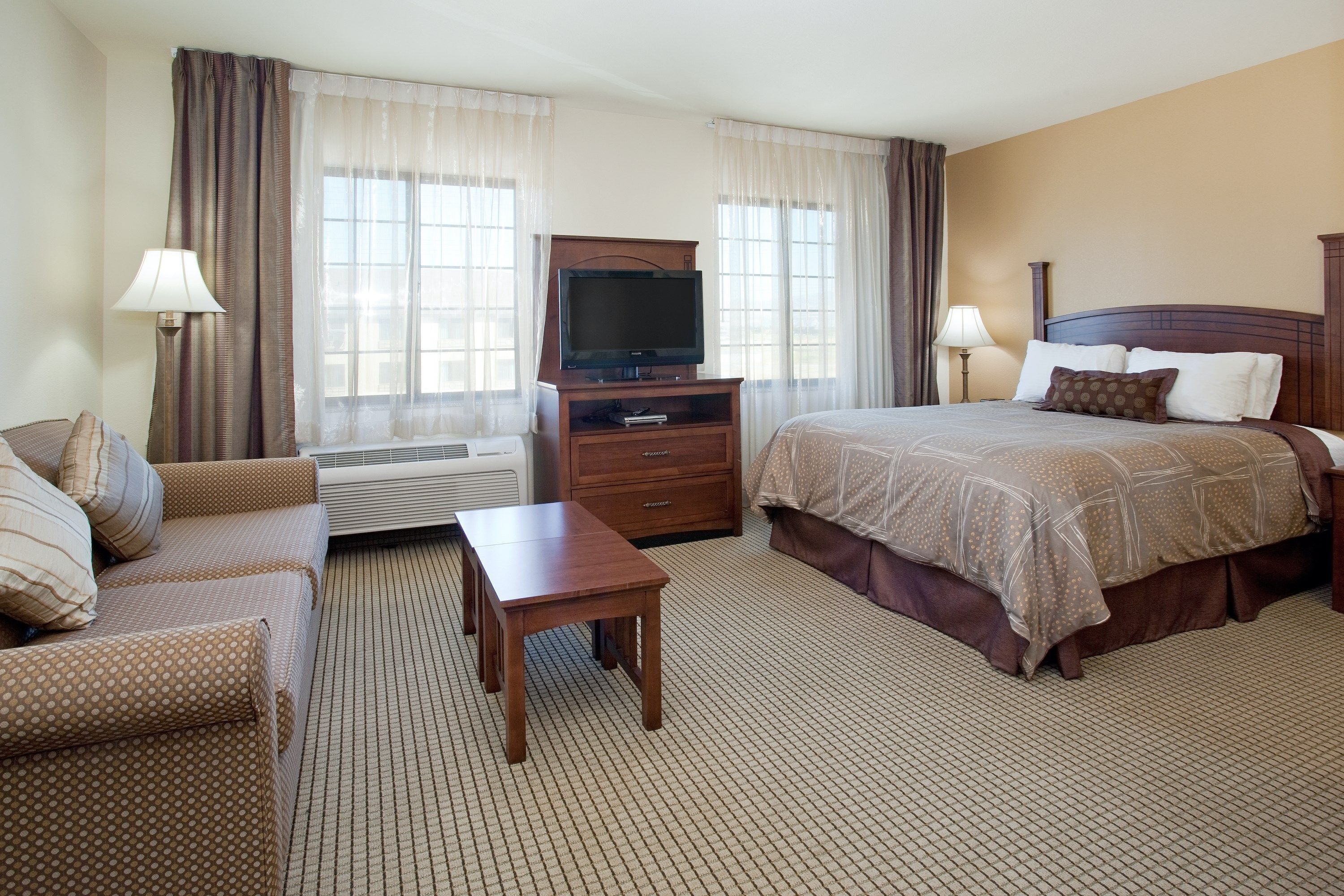 A hotel room with a bed, a TV on a wooden stand, a sofa, a small table, and two lamps.