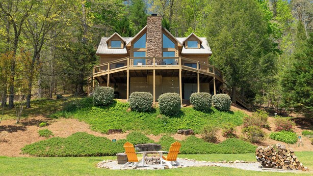 Un chalet doté d’une cheminée en pierre, de balcons en bois et d’une terrasse entourée d’arbres.