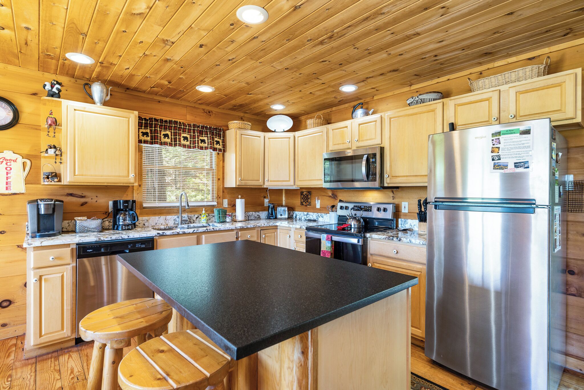Une cuisine rustique aménagée dans une cabane en bois, avec un îlot central, des appareils en acier inoxydable et des tabourets en bois.