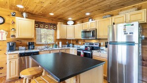 Une cuisine rustique aménagée dans une cabane en bois, avec un îlot central, des appareils en acier inoxydable et des tabourets en bois.