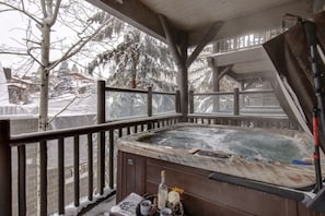 Uma banheira de hidromassagem em um alpendre com vista para árvores e casas cobertas de neve.
