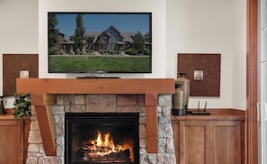 A fireplace with a stone surround, a flat-screen TV mounted above it, and a view of a house in the background.