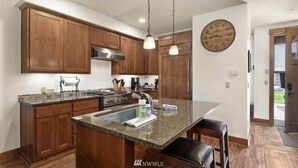 Una cocina con armarios de madera, encimera de granito, pileta de acero inoxidable y un reloj en la pared.