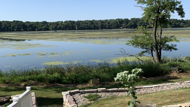 A stone staircase leading to a wooden deck overlooking a lake with a grassy area and a tree. - WELCOME!  Are you looking to get away, to disconnect and relax? Look no further. (Montello)
