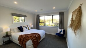 Ein Schlafzimmer mit einem Bett, zwei Nachttischen, einem Sessel, einem Fenster und Blick auf Grünfläche.