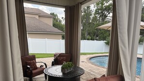 A covered patio area with outdoor furniture, a round table, and a view of a swimming pool and a white fence. - Beautiful home with pool (Orange Park)