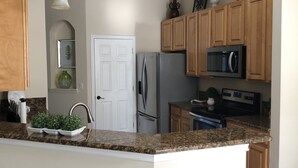 A kitchen with granite countertops, wooden cabinets, stainless steel appliances, and a white door. - Beautiful home with pool (Orange Park)