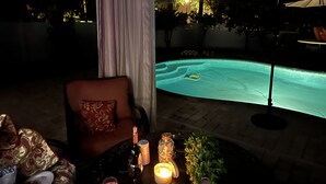 An outdoor pool area with a chair and table, a bottle of wine, and candles. - Beautiful home with pool (Orange Park)