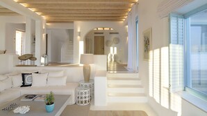 Een ruime woonkamer met een houten plafond, een zithoek, een bijzettafeltje met decoratieve objecten en uitzicht op een trap die naar een deur leidt.