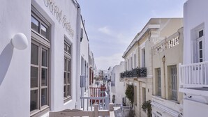 Une rue étroite bordée de bâtiments blancs, de balcons et d’une enseigne indiquant « Pandora ».