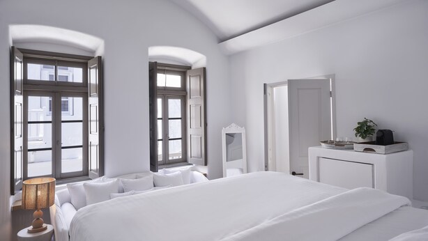 Une chambre d’hôtel moderne avec un grand lit, une table de chevet avec une lampe, un miroir et une commode agrémentée d’une plante.