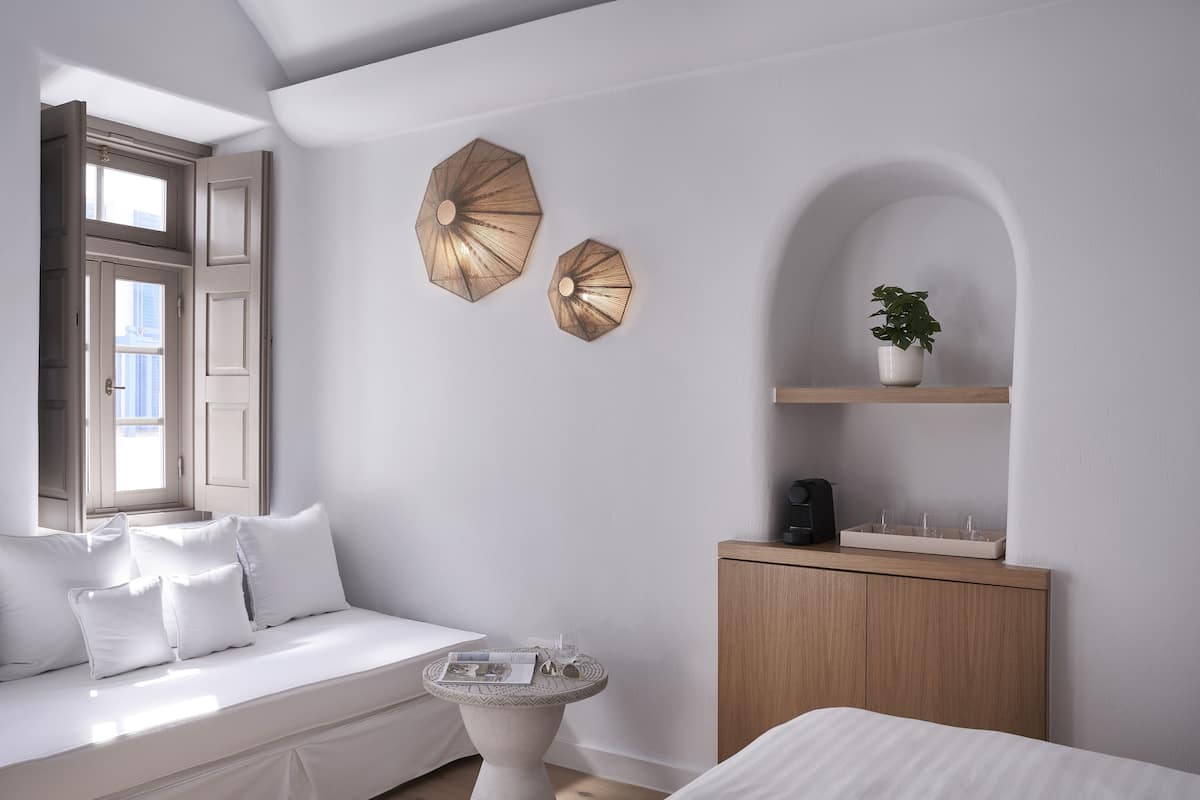 Una habitación con un sofá blanco, una pequeña mesa redonda, un aparador de madera y dos sombrillas colgadas en la pared.