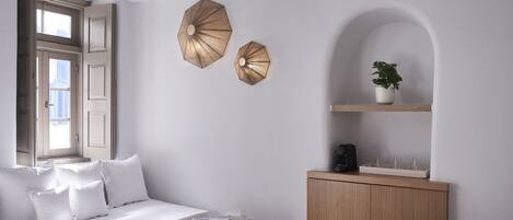 Una habitación con un sofá blanco, una pequeña mesa redonda, un aparador de madera y dos sombrillas colgadas en la pared.