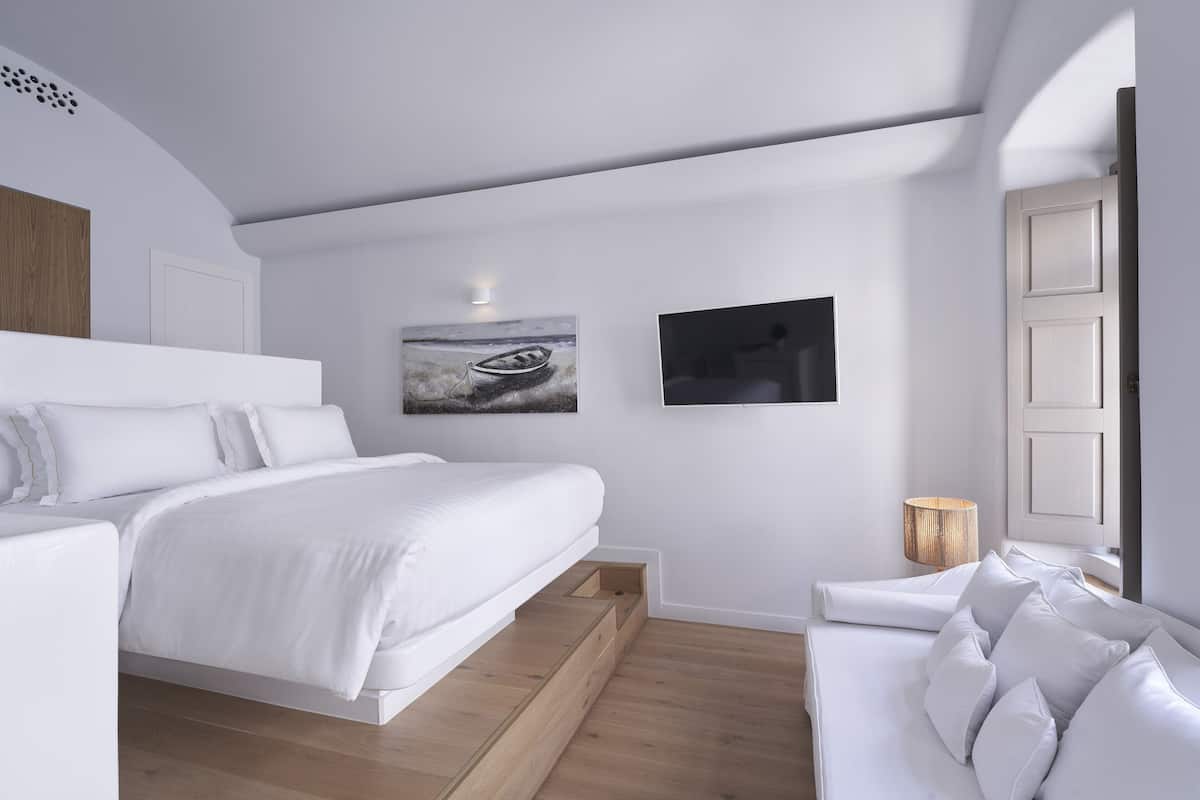 Un dormitorio moderno con cama, sofá, una obra de arte colgada en la pared y una ventana.