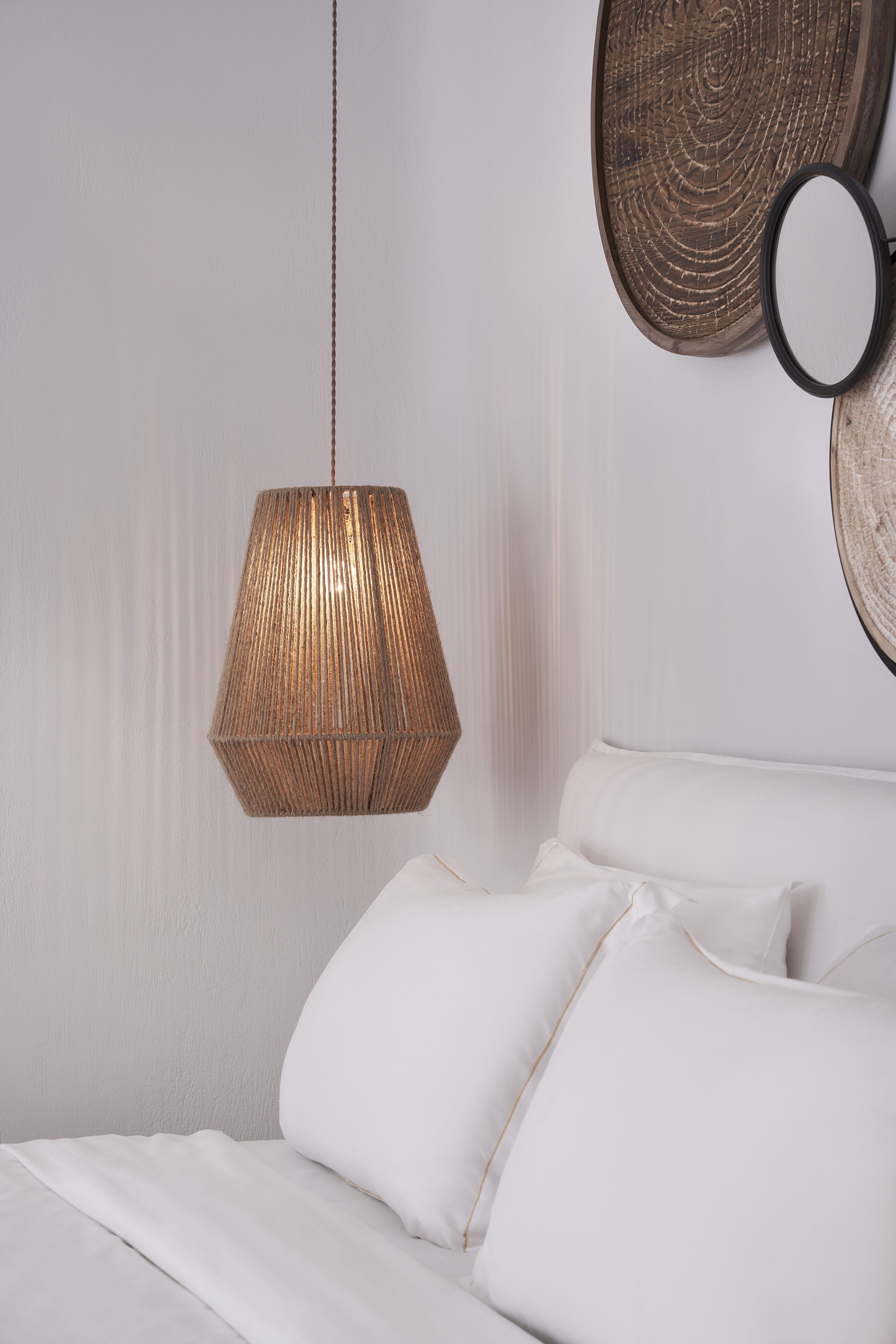 A bed with white linens and a hanging woven light fixture.