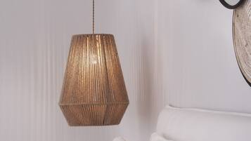 A bed with white linens and a hanging woven light fixture.