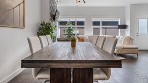 Un coin repas avec une grande table en bois, des chaises rembourrées, une plante en pot et un lustre moderne.