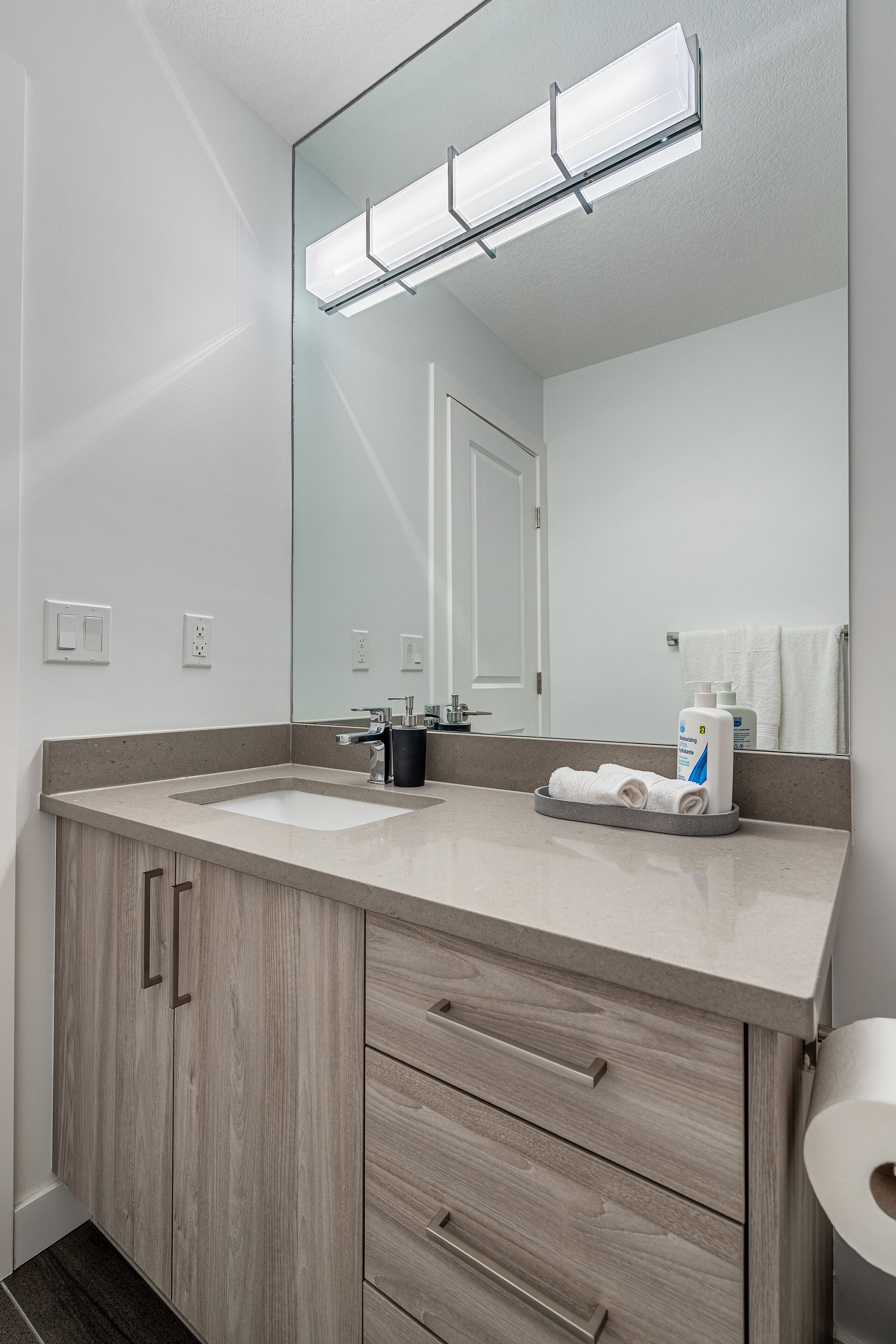 A modern bathroom with two sinks, a large mirror, and a toilet paper holder.