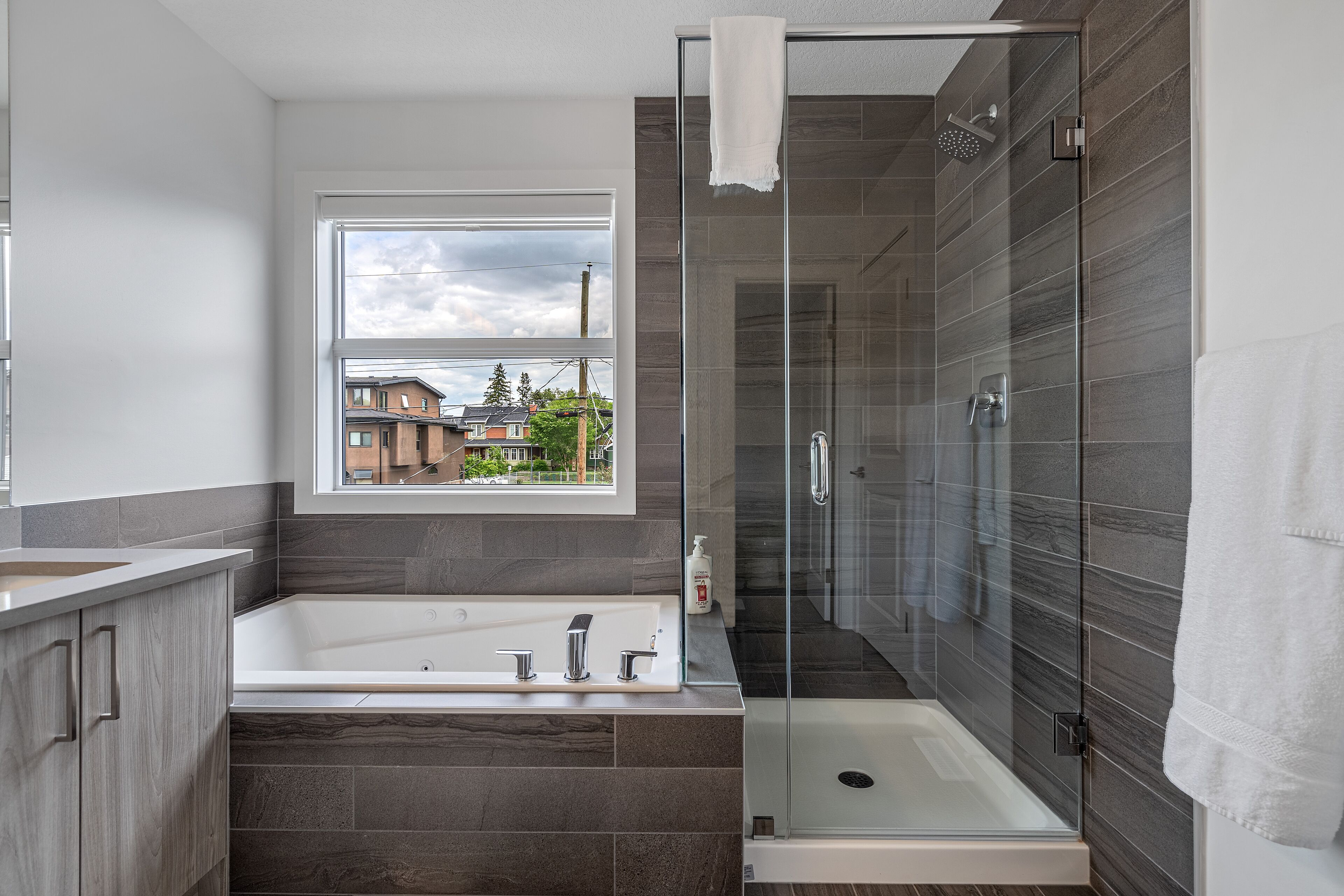 A modern bathroom with a large bathtub, a glass-enclosed shower, and a window providing a view of the outside.