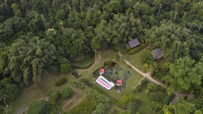 Luchtbeeld van een pand met zwembad, twee gebouwen en omliggend dicht bos.
