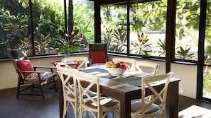 Een eethoek met een tafel voor vier personen, omringd door stoelen met kussens, en een schaal fruit op de tafel.