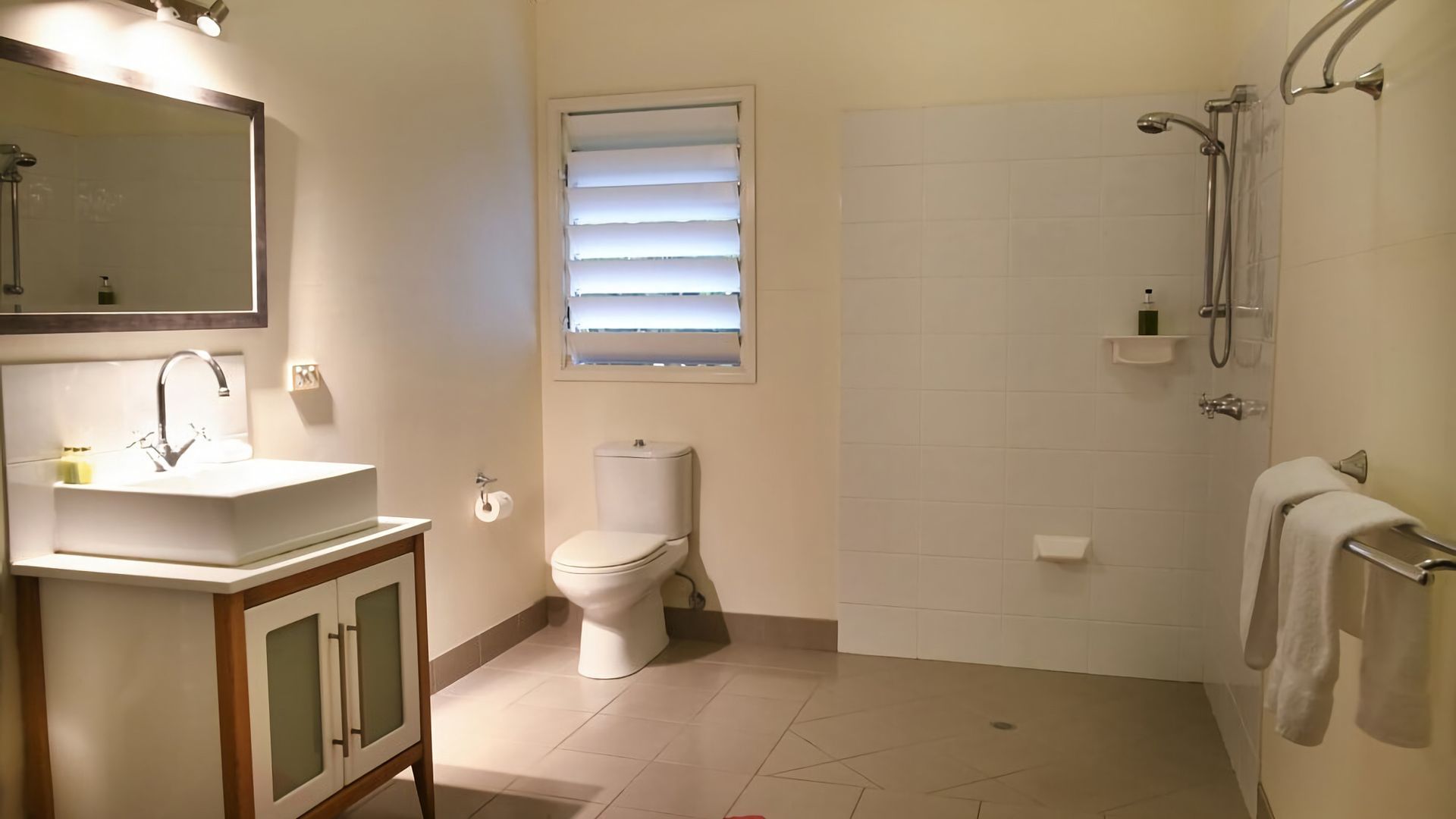 Un baño con lavabo, inodoro, ducha y una ventana con persianas.