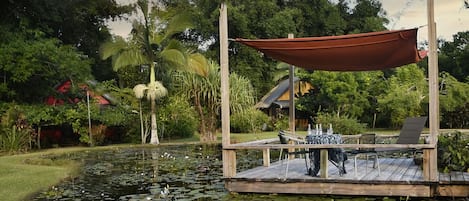 A wooden dock with a table and chairs, surrounded by a pond with lily pads.