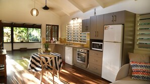 A modern kitchen with a dining area, large windows, and a view of greenery.