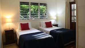 Een hotelkamer met twee bedden, een raam met uitzicht op groen en een deur met gordijnen.