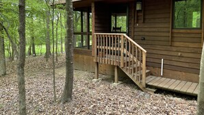 A wooden cabin with a wooden deck and a staircase leading to a covered porch. - Cabin amongst the trees (Waxhaw)