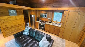 A compact cabin-style kitchen with wooden cabinetry, a built-in microwave, a stove, and a refrigerator. - Cabin amongst the trees (Waxhaw)
