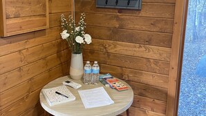 A wooden cabin interior with a round table, a vase of flowers, two water bottles, a remote control, a notebook, and some documents. - Cabin amongst the trees (Waxhaw)