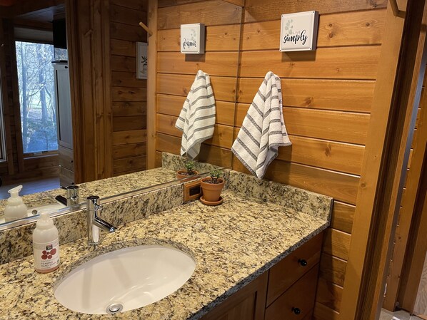 Une salle de bain avec un lambris en bois, un comptoir en granit, un lavabo, deux serviettes et deux panneaux affichés sur le mur.