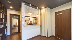 Un área de recepción con un mostrador de madera, una barra con un cartel, una estantería y una puerta de madera con la etiqueta "ROOM 1".