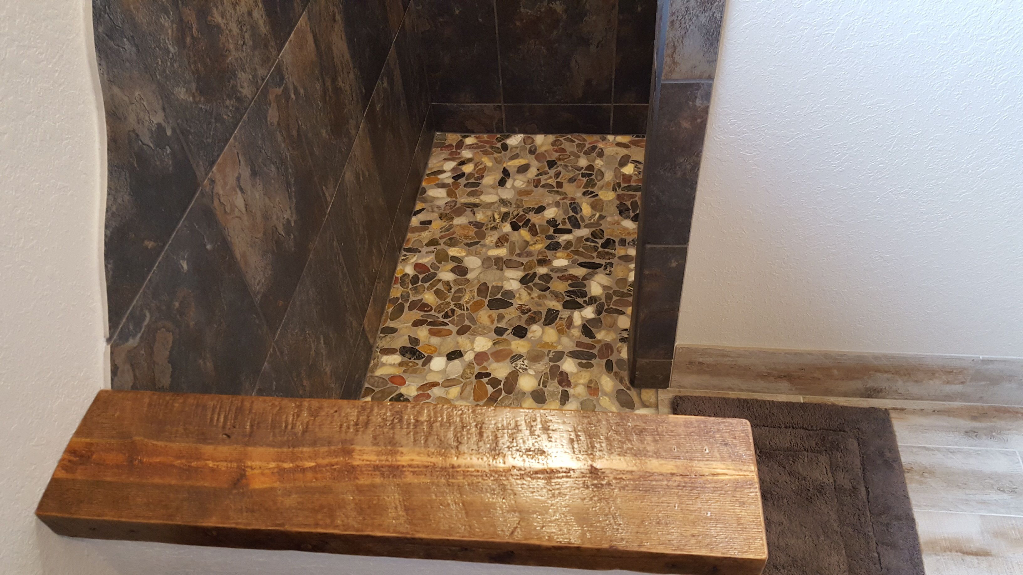 A wooden bench with a stone mosaic floor leading to a dark tiled area.