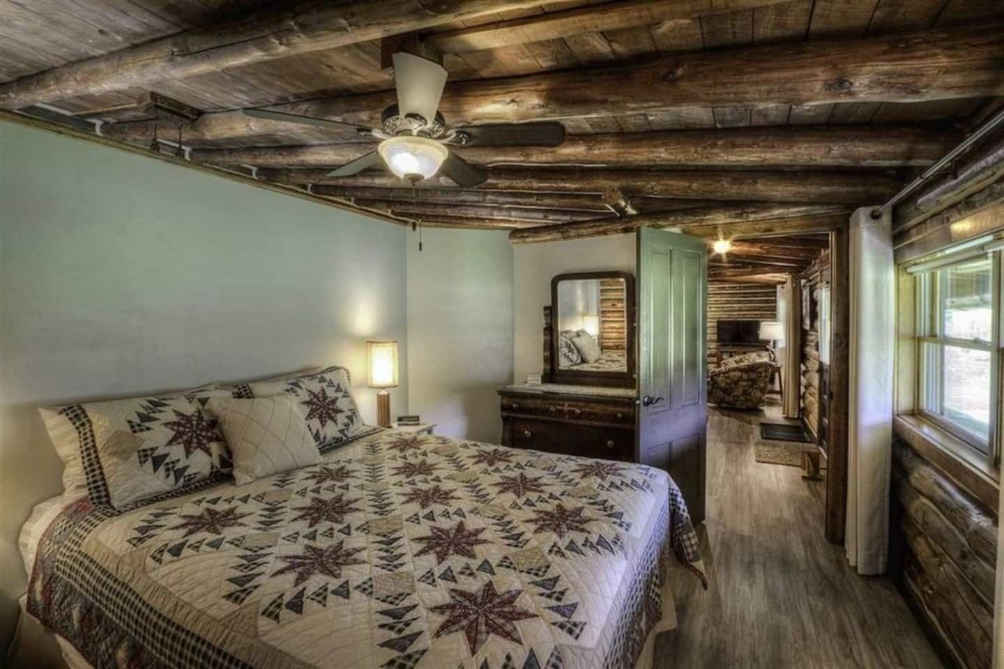 Una camera da letto rustica con un letto grande, una cassettiera, uno specchio e una ventola a soffitto.