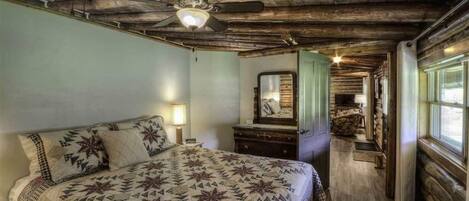 Una camera da letto rustica con un letto grande, una cassettiera, uno specchio e una ventola a soffitto.