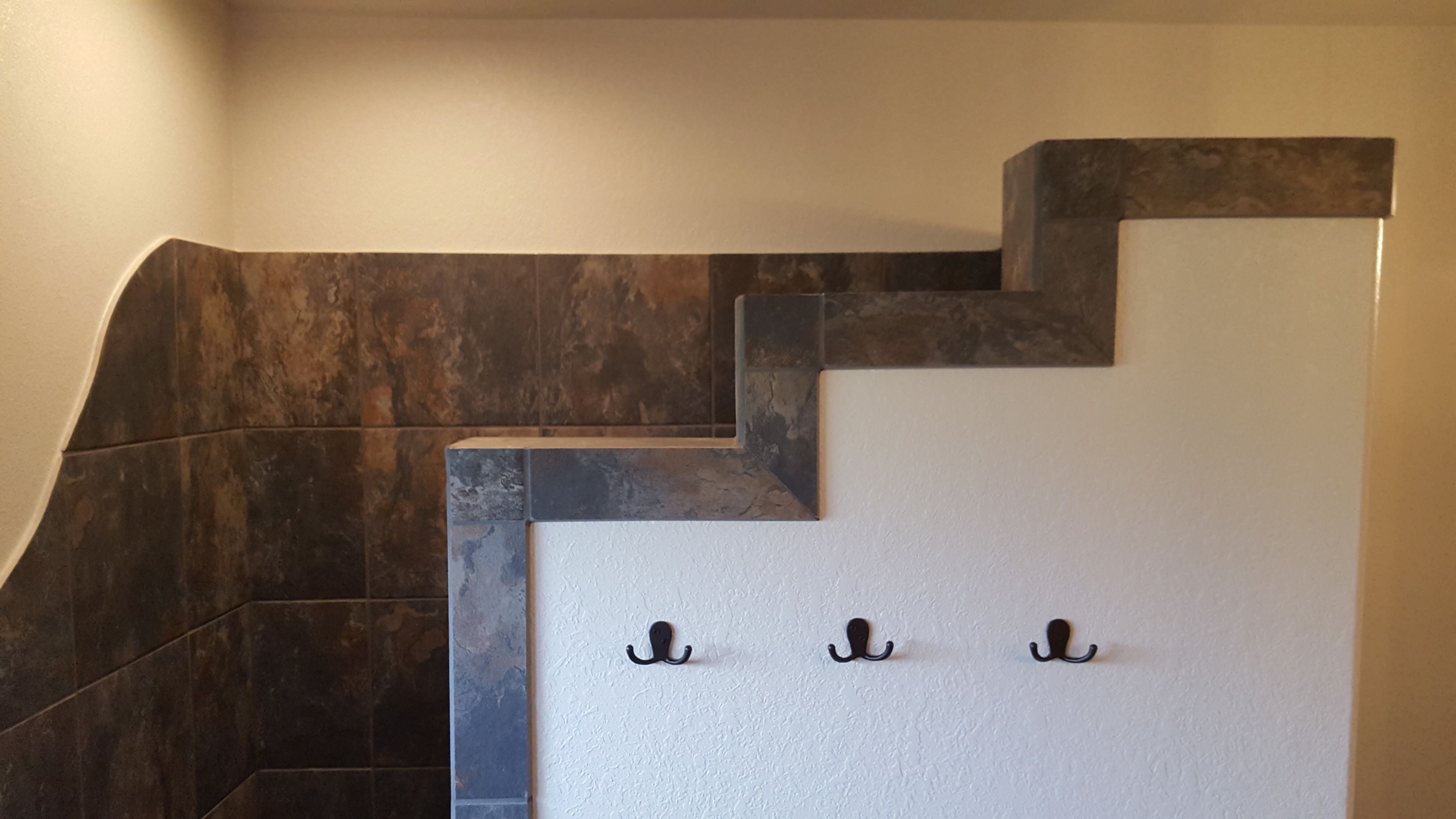 A staircase with dark, textured steps and a white wall with three black hooks.