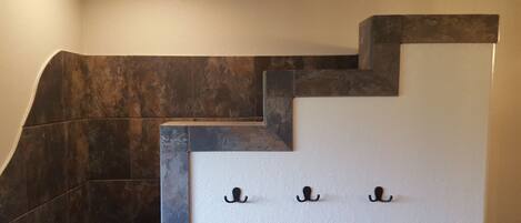 A staircase with dark, textured steps and a white wall with three black hooks.