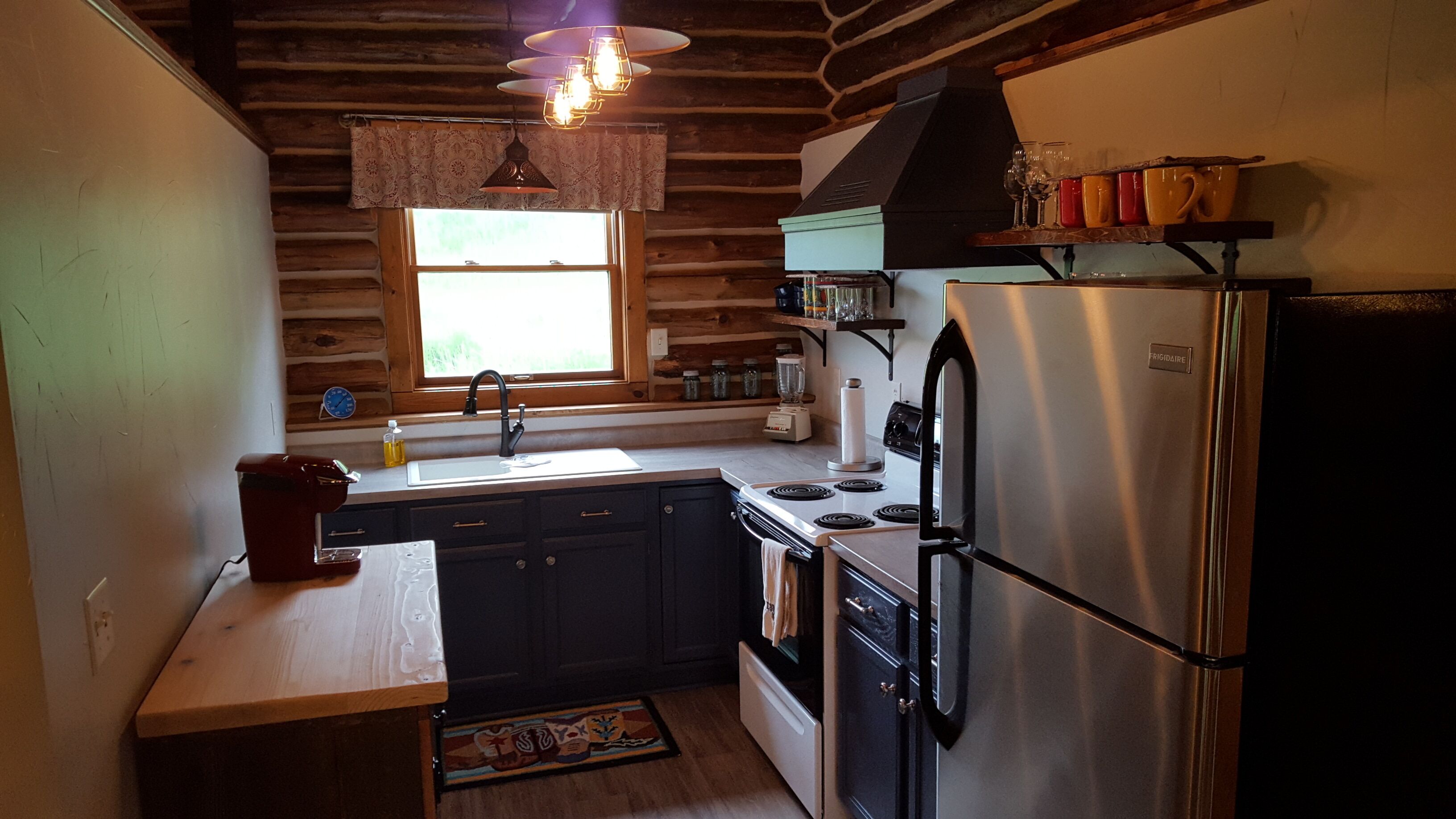 A compact kitchen with wooden walls, a stainless steel refrigerator, a stove, and a sink.