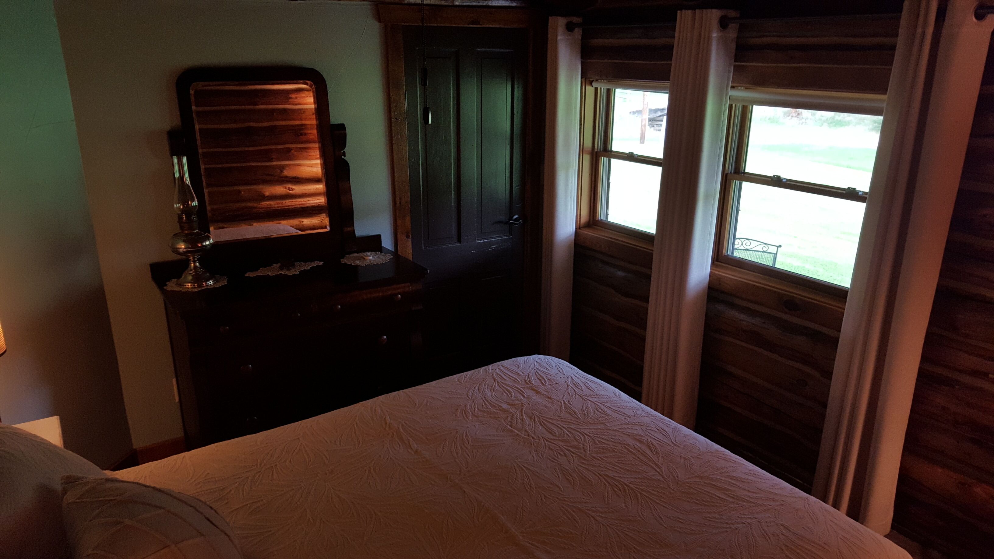 Una habitación con cama, cómoda con espejo y ventana con cortinas.