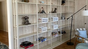Una habitación con paredes de paneles de madera, un estante blanco con varios objetos y una mesa redonda de madera con un florero.