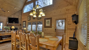 A wooden interior with a dining table, chairs, a fireplace, and a TV mounted on a stone wall. - Riverfront Cabin w/ Private Dock, Putting Green, Game Room!  3.5mi 2 Blue Ridge (Blue Ridge)