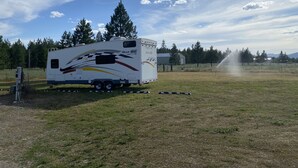 Veículo recreativo (RV) estacionado em um campo gramado, com céu claro e árvores ao fundo.