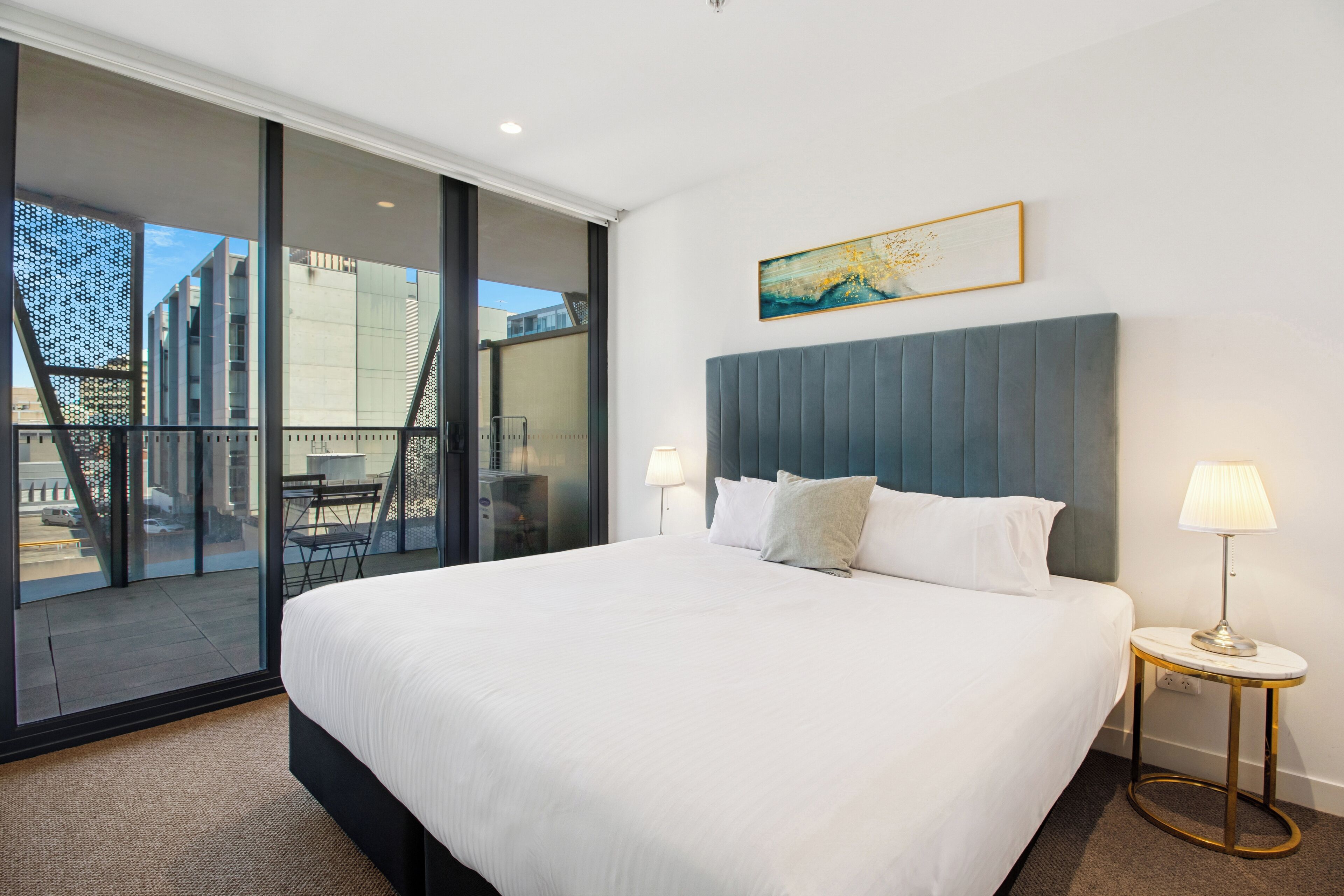 Habitación de hotel con una cama grande, un balcón con vistas, un cuadro en la pared y una lámpara en la mesita de noche.