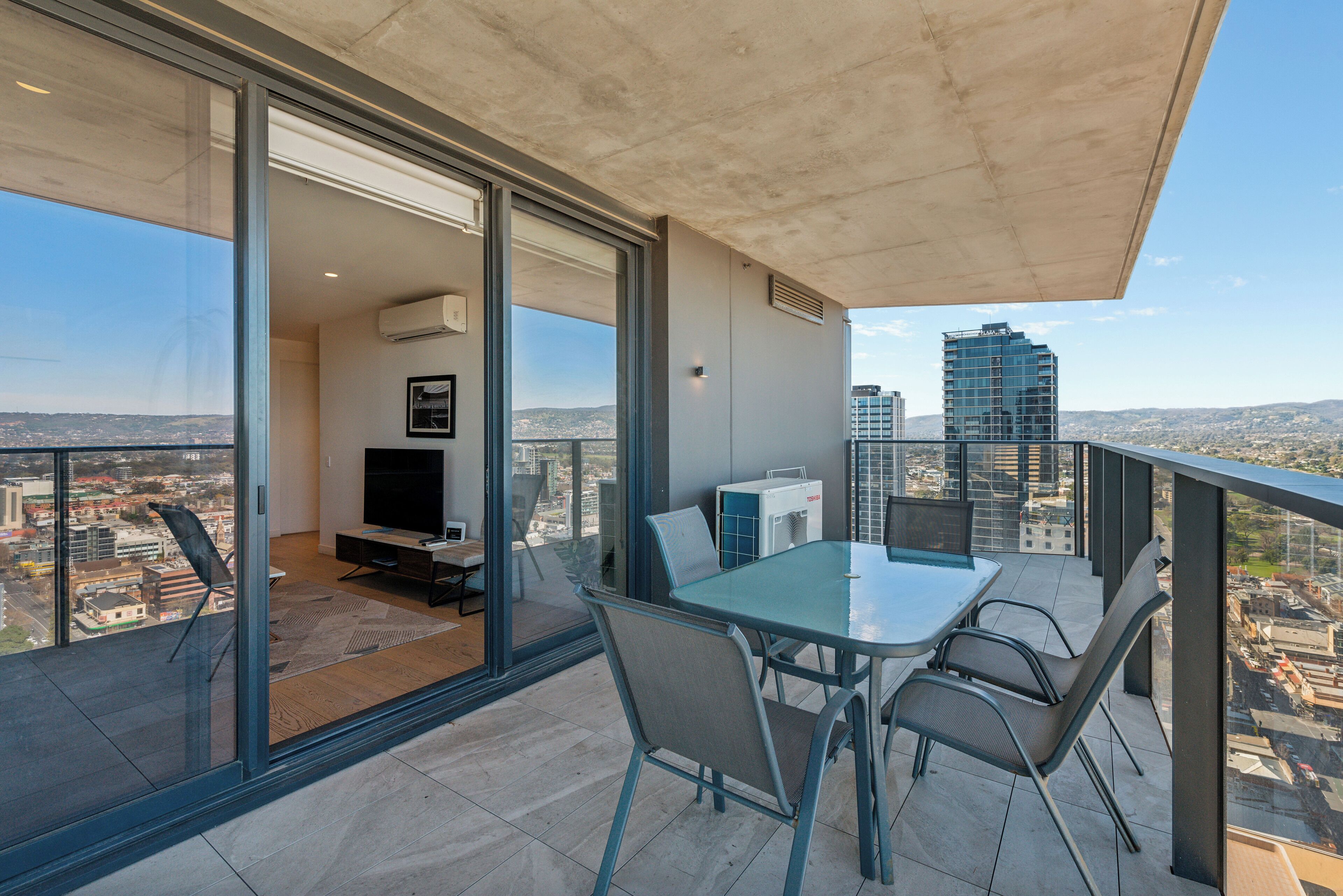 A balcony with a glass door, a table with chairs, a TV, and an air conditioning unit.