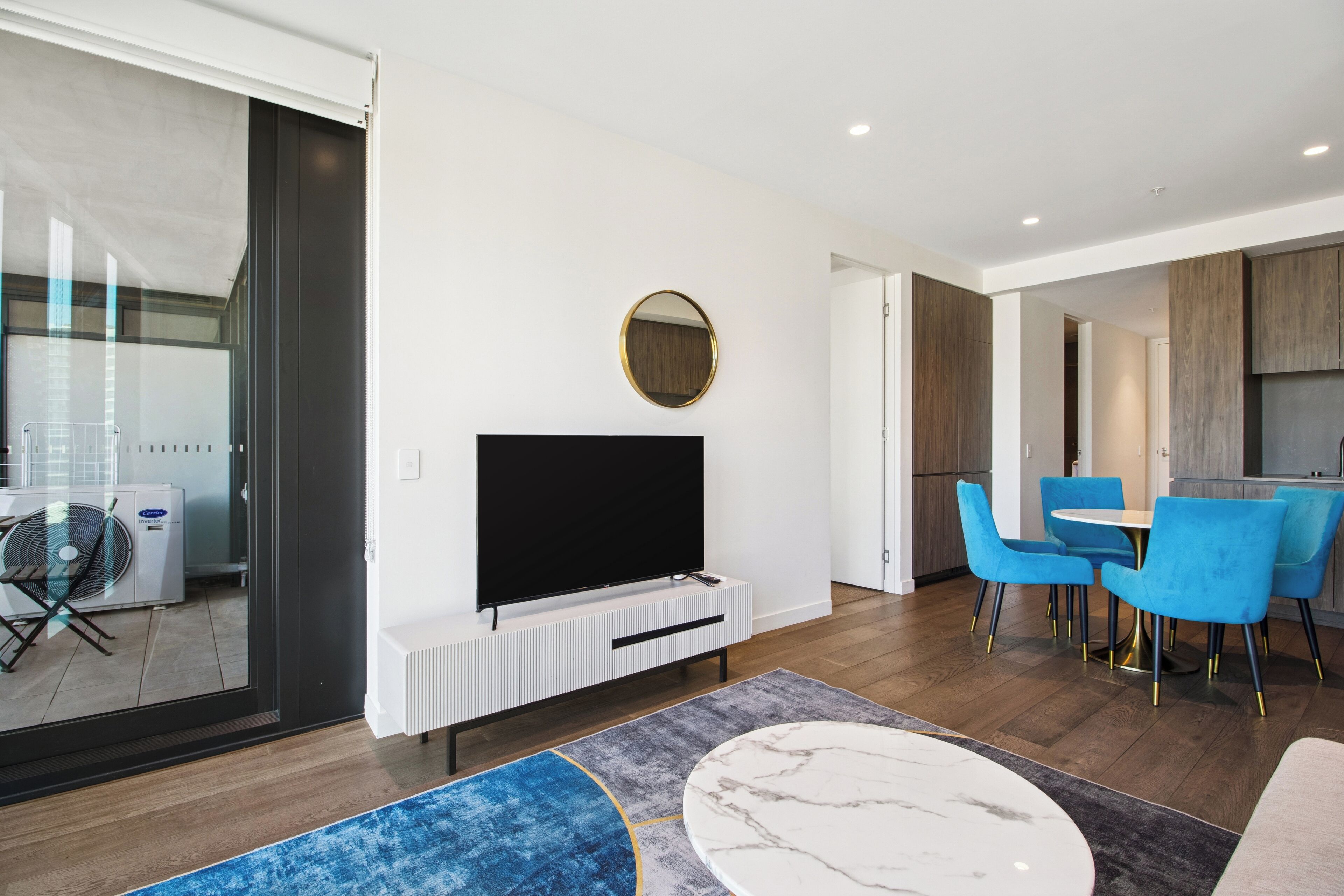 A modern living room with a flat-screen TV, blue chairs, a round table, and a large mirror.