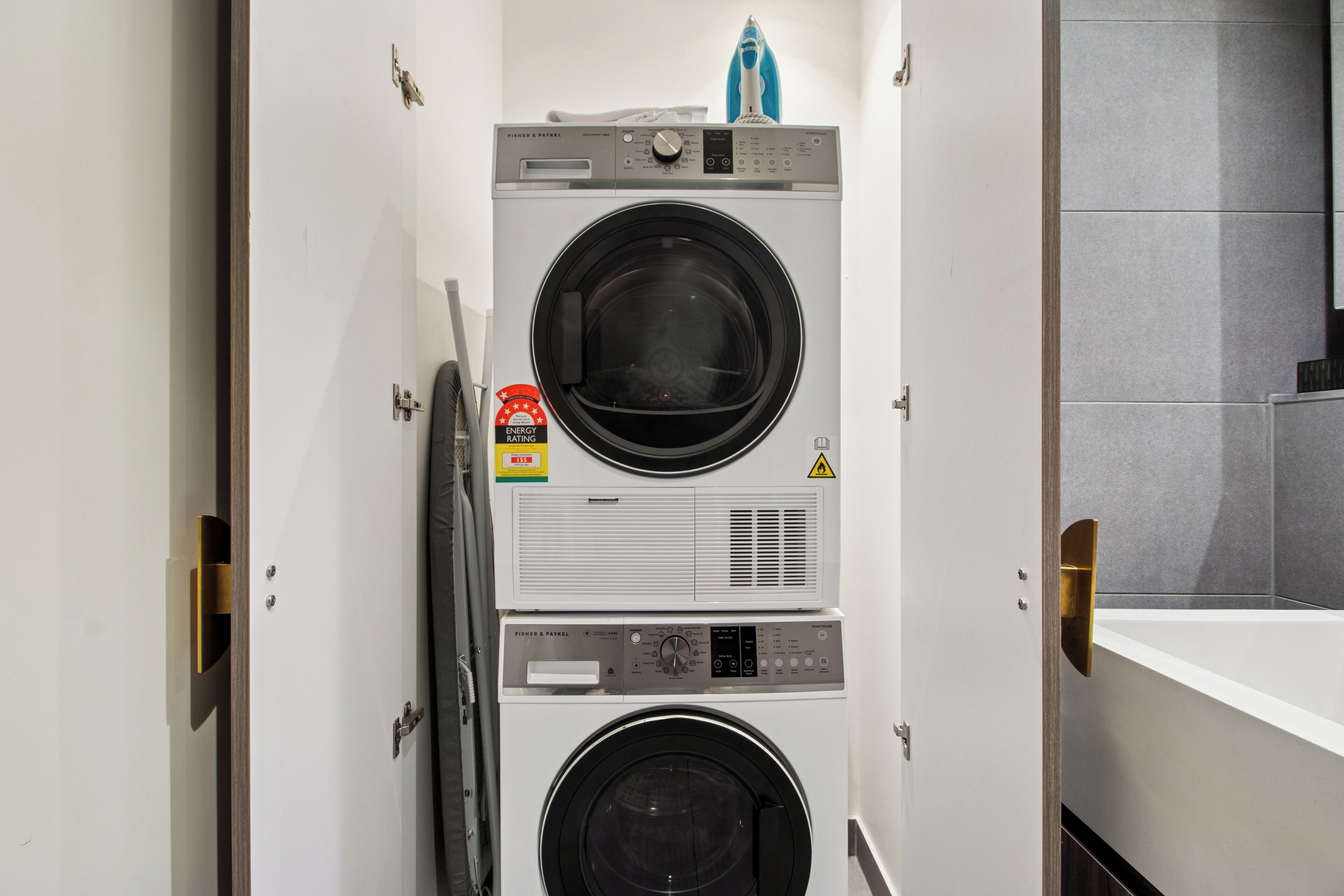 A stacked washer and dryer unit with a control panel, a caution label, and a water meter.