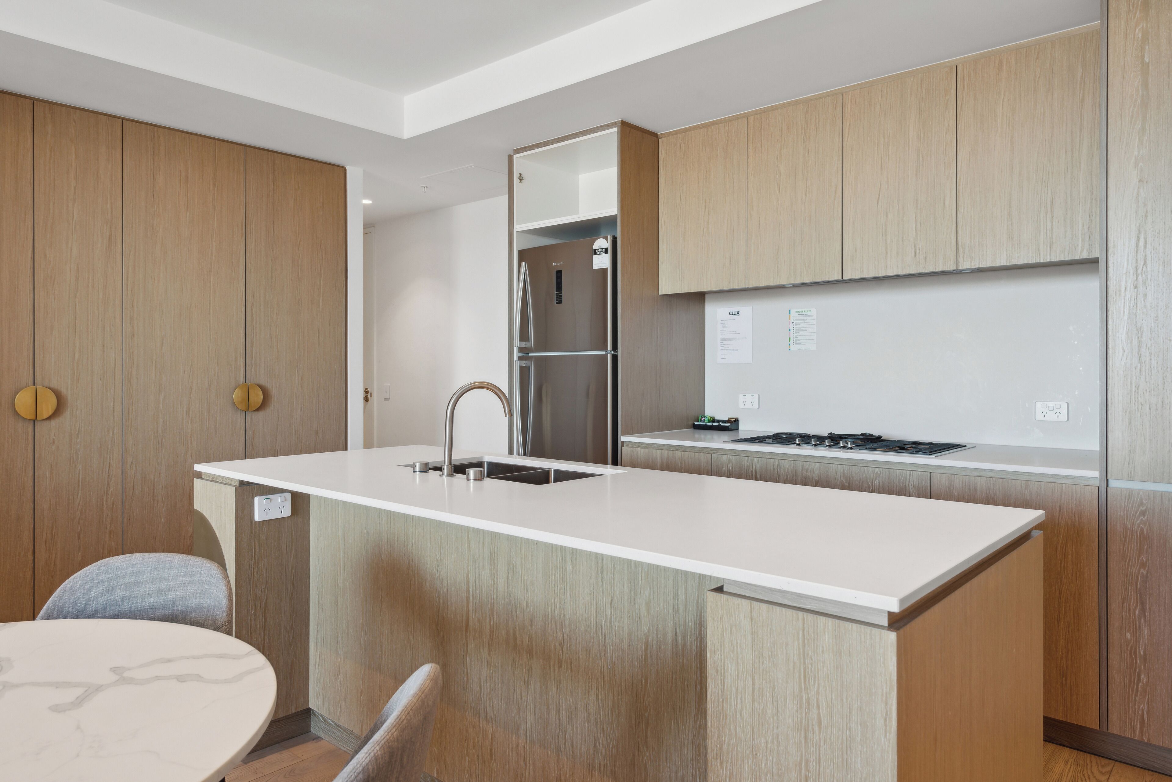 A modern kitchen with wooden cabinets, a stainless steel refrigerator, a built-in stove, and a round dining table.